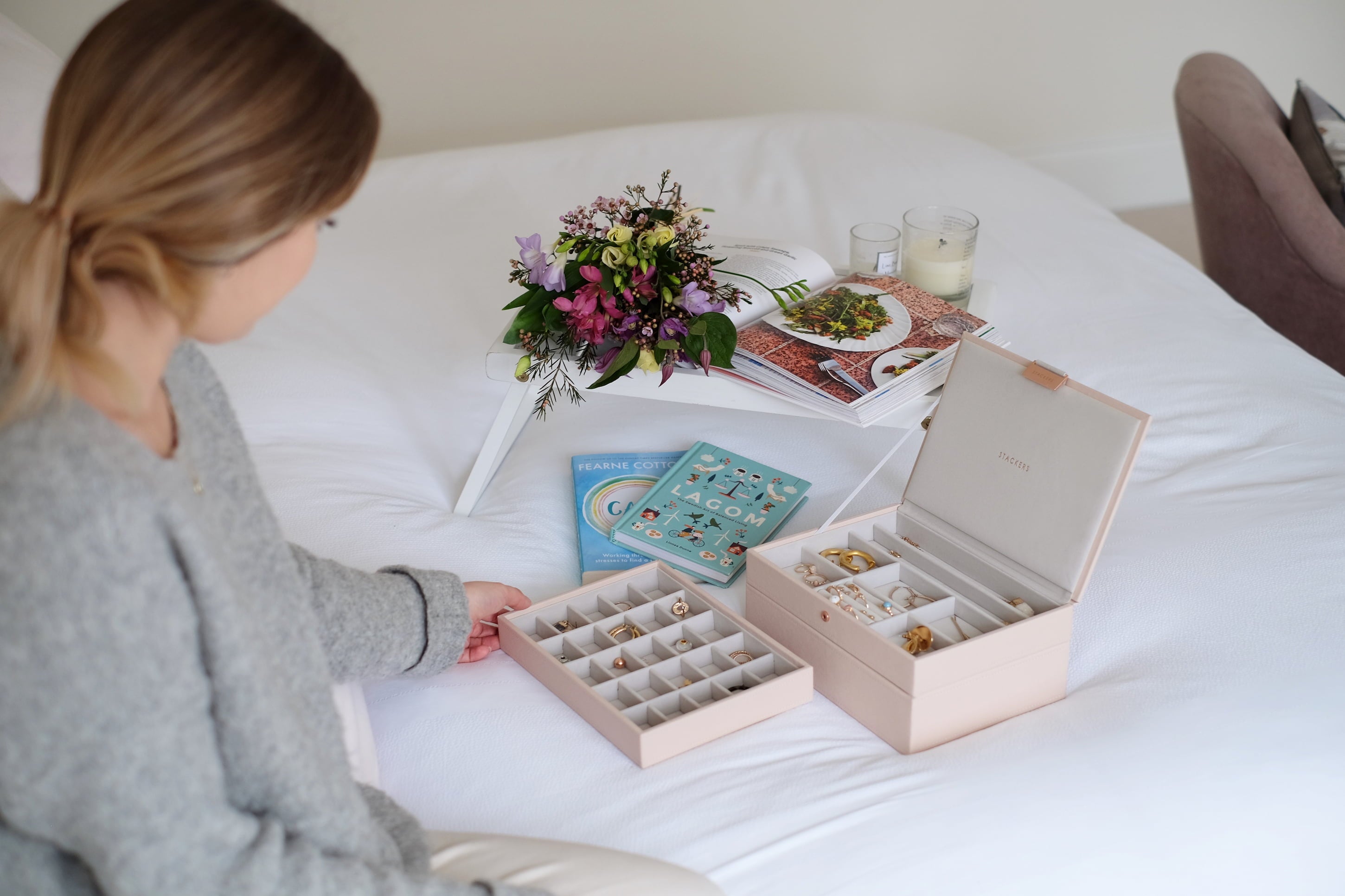 Woman sitting on a bed with jewelry boxes and a flower arrangement on a Mother's Day Morning